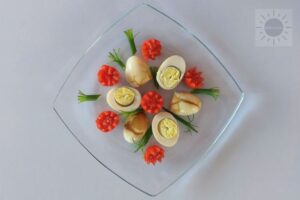 Spiced Eggs Haminados Cut In Half On A Serving Dish Decorated With Tomato Flowers And Scallion Leaves.