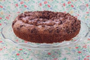 Cinnamon Swirl Cake On A Glass Cake Stand That's On A Flowered Cloth.