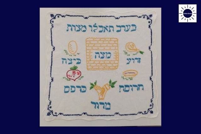 An Embroidered Matzah Cover With The Seder Plate Symbols Written In Hebrew.