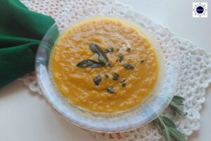 Pumpkin Leek Soup With A Sage Garnish In A Glass Bowl On A Lace Placemat With A Decorative Napkin And Fresh Sage Leaves On The Side.