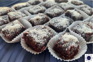 Glazed Wholegrain Coconut Brownies In Cupcake Holders Spread On A Decorative Pleated Cloth.