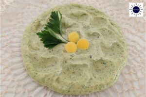 Vegan Parsley Tahini Spread Decorated With Lemon Peel Circles To Form A Flower And Parsley Leaves On A Serving Plate On Top Of A Doily