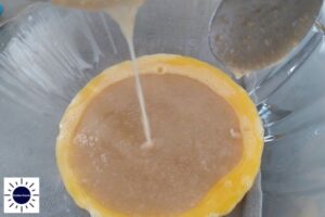 Pouring Part Of The Hot Oat And Honey Mixture Into The Egg Yolks That Are In A Bowl.