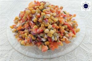 Vegan No-Mayo Crunchy Corn Salad On A Serving Plate On A Lace Cloth With The Kosher Create Sun Logo In The Upper Right Corner.
