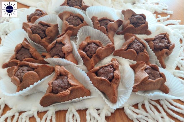 Wholegrain Almond Maple Cocoa Hamantashen In Cup Cake Holders On Cloth With Tassels In Front.