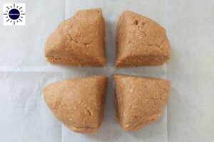 Ball Of Cookie Dough Divided Into Four Parts On Baking Sheet.