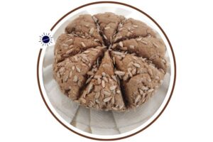 Wholegrain Sunflower Seed Soda Bread On Top Of A Folded Textured Cloth Within A Decorative Circle Frame With The Graphic The Kosher Create Sun Logo On The Upper Left Of The Circle.