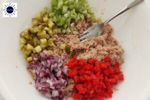 A Closeup Of Cubed Vegetables Added To The Mashed Tuna With A Fork In A Bowl And With The Kosher Create Sun Logo In The Upper Left Corner.