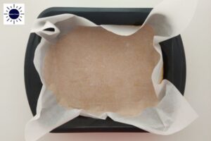 The Rolled Out Peanut Butter Dough In The Bottom Of A Baking Pan Covered With A Baking Sheet With The Kosher Create Sun Logo In The Upper Left Corner.