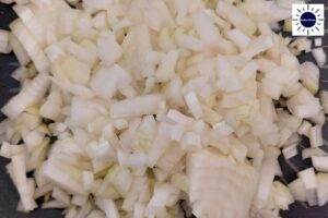 A Closeup Of Onions Diced Into Small Cubes With The Kosher Create Sun Logo In The Upper Right Corner.