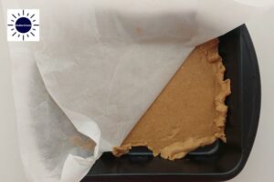 Peanut Butter Dough On Bottom Of Baking Pan With The Top Baking Sheet Partially Peed Away With The Kosher Create Sun Logo In The Upper Left Side.