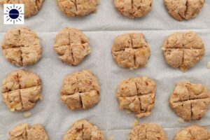 Closeup Of Flattened Dough Balls With A Plus Cut In The Middle Spread Out On A Baking Sheet And With The Kosher Create Sun Logo In The Upper Left Corner.
