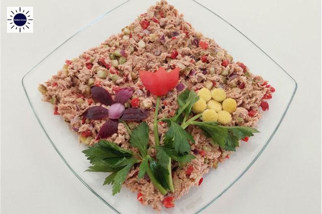 Mediterranean No-Mayo Dairy-Free Tuna Salad On a Diamond Shaped Glass Serving Plate Adorned With Three Flowers Carved Out Of An Onion A Bell Pepper And Lemon Skin With Celery Leaves On The Stem And With The Kosher Create Sun Logo In The Upper Left Corner.