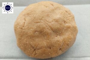 A Ball Of Dough On A Baking Sheet With The Kosher Create Sun Logo In The Upper Left Corner.