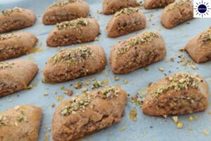 Blended Pistachio Sprinkled On The Cookies On A Baking Sheet With The Kosher Create Sun Logo In The Upper Right Corner.