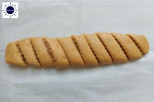 The Cookie Roll Sliced Diagonally Into One Inch Wide Pieces On A Baking Sheet With The Kosher Create Sun Logo In The Upper Left Corner.