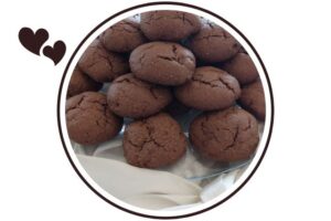 Wholegrain Cocoa Maple Mocha Cookies On A Glass Serving Plate On Top Of Bunched Silky Material With a Decorative Silky Large Bow In Front That's Suited For Dessert In A Decorative Circle Adorned With Two Graphic Hearts On The Side.

