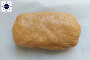 Dough Made Into An Oblong Shape On A Baking Sheet With The Kosher Create Sun Logo In The Upper Left Corner.
