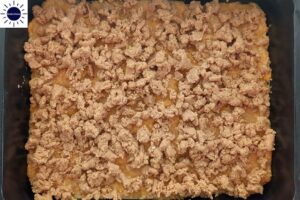 Grated Dough Scattered On Top Of Apricot Filling In The Baking Pan With The Kosher Create sun Logo In The Upper Left Corner.