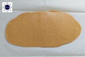 The Dough Rolled Into A Long Oval Shape On A Baking Sheet With The Kosher Create Sun Logo In The Upper Left Corner.