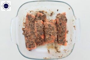 Baked Salmon Within A Square Glass Baking Dish With The Kosher Create Sun Logo In The Upper Left Side.