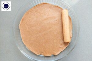 The Dough Crust In A Round Glass Pie Dish Smoothed Out With A Small Rolling Pin With The Kosher Create Sun Logo In The Upper Left Corner.