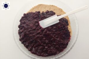 The Filling Spread On The Baked Pie Crust With A Spatula In A Round Glass Pie Dish With The Kosher Create Sun Logo In The Upper Left Corner.