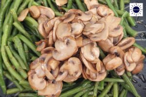 A Closeup Of The Sauteed Mushrooms On Top Of The Green Beans With The Kosher Create Sun Logo In The Upper Right Corner.