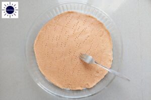 The Dough Crust In A Round Glass Pie Dish Perforated With A Fork With The Kosher Create Sun Logo In The Upper Left Corner.