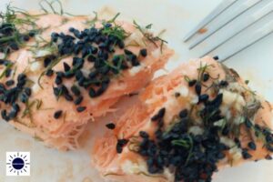A Closeup Of A Slice Of Fish With A Fork And With The Kosher Create Sun Logo In The Lower Left Corner