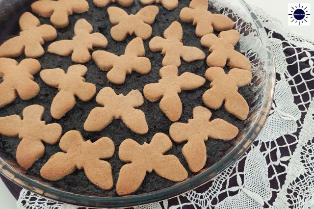 A Closeup Of A Wholegrain Lemony Blueberry Pie Decorated With Blueberry Cookies On Top In A Round Glass Pie Dish On Top Of A Lace Cloth With Blueberry Ornaments And With The Kosher Create Sun Logo In The Upper Right Corner.