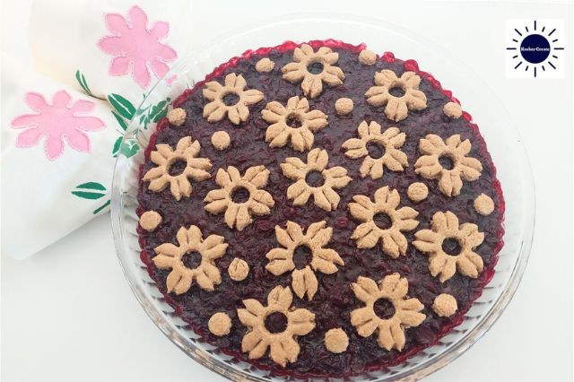 Wholegrain Mapley Cherry Pie In A Round Glass Baking Dish Decorated With A Delicate Cherry Blossom Cut Cookies Motif With A Decorative Napkin Folded In The Upper Left Side Adorned With Two Flowers And With The Kosher Create Sun Logo In The Upper Right Corner.