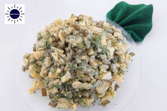 Vegan No-Mayo Baked Potato Salad On A Round Glass Dish With A Decorative Napkin In The Shape Of A Leaf On The Right Upper Side And The Kosher Create Sun Logo On The Upper Left Side.