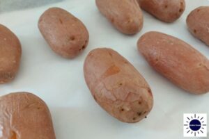 A Closeup Of Baked Potatoes On A Baking Sheet With The Kosher Create Sun Logo In The Bottom Right Corner.