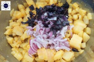 A Closeup Of The Sliced Onions And Basil Added To The Cubed Potato Mixture With The Kosher Create Sun Logo In The Upper Left Corner.