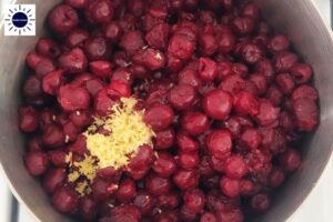 A Closeup of Cherries And Lemon Ina Pot Before Cooking With The Kosher Create Sun Logo In The Upper Left Corner.
