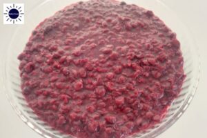 The Cherry Filling Spread Over Pie Crust In A Round Glass Pie Dish With The Kosher Create Sun Logo In The Upper Left Side.