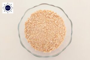 A Closeup Of Coarsely Chopped Cashew Nuts In A Glass Bowl With The Kosher Create Sun Logo In The Upper Left Side.