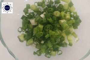 A Closeup Of The Diced Scallions In A Glass Bowl With The Kosher Create Sun Logo In The Upper Left Corner.