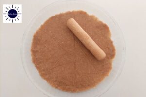 The Pie Crust In A Round Glass Dish Smoothed Out With A Small Rolling Pin With The Kosher Create Sun Logo In The Upper Left Corner.