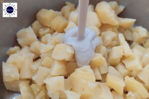 A Closeup Of The Dressing Being Poured On The Cubed Potatoes With The Kosher Create Sun Logo In The Upper Left Side.