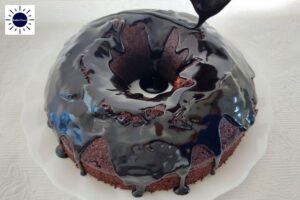 The Dairy-Free Maple Cocoa Glaze Being Pored Onto A Cocoa Cake With The Kosher Create sun Logo In The Upper Left Corner.
