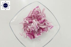 Sliced Onions Mixed With Salt In A Glaa Dish With The Kosher Create Sun Logo In The Upper Left Corner.