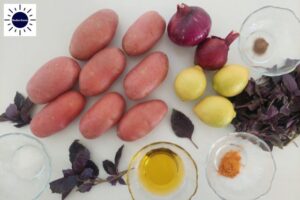 Mediterranean Baked Purple Potato Salad Recipe Ingredients On A Surface With The Kosher Create Sun Logo In The Upper Left Corner.