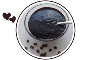 Almond Mocha Glaze In A Glass Dish With Serving A Spoon And With Several Coffee Beans Scattered Beside It. That's Suited For Dessert In A Decorative Circle Adorned With Two Graphic Hearts On The Side.