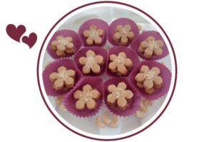 Wholegrain Lemony Cashew Cookies Stacked In Colorful Cupcake Holders Arranged On A Serving Plate Like A Flower With Assorted Cashew Nuts Around That's Suited For Dessert In A Decorative Circle Adorned With Two Graphic Hearts On The Side.
