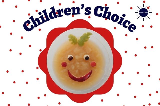 The Title Children's Choice With The Graphic Applesauce And Lemon Zest Showcased As A Happy Face Within A Ruffley Circle With A Polka dot Background And The Kosher Create Sun Logo In The Upper Right Corner.